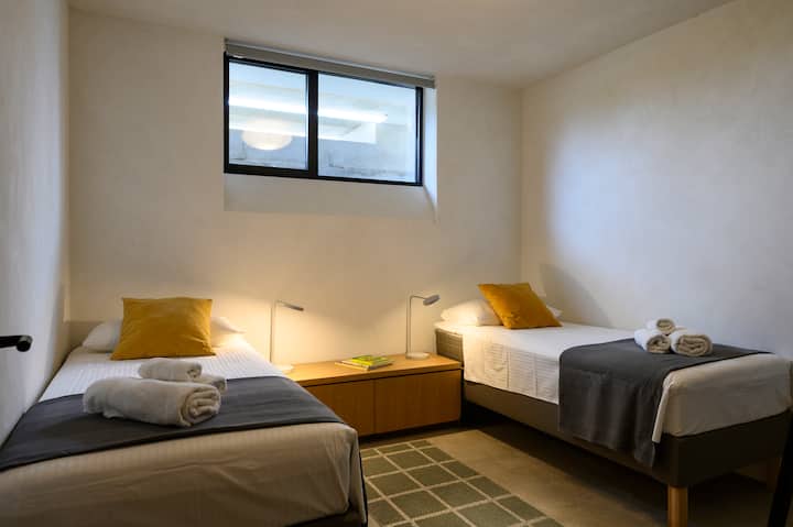 Hiki ndicho chumba kidogo cha kulala kwenye chumba cha chini. Madirisha pia yanaangalia magharibi.  Haijaonyeshwa ni rafu ya mbunifu ya kuning 'inia nguo. 