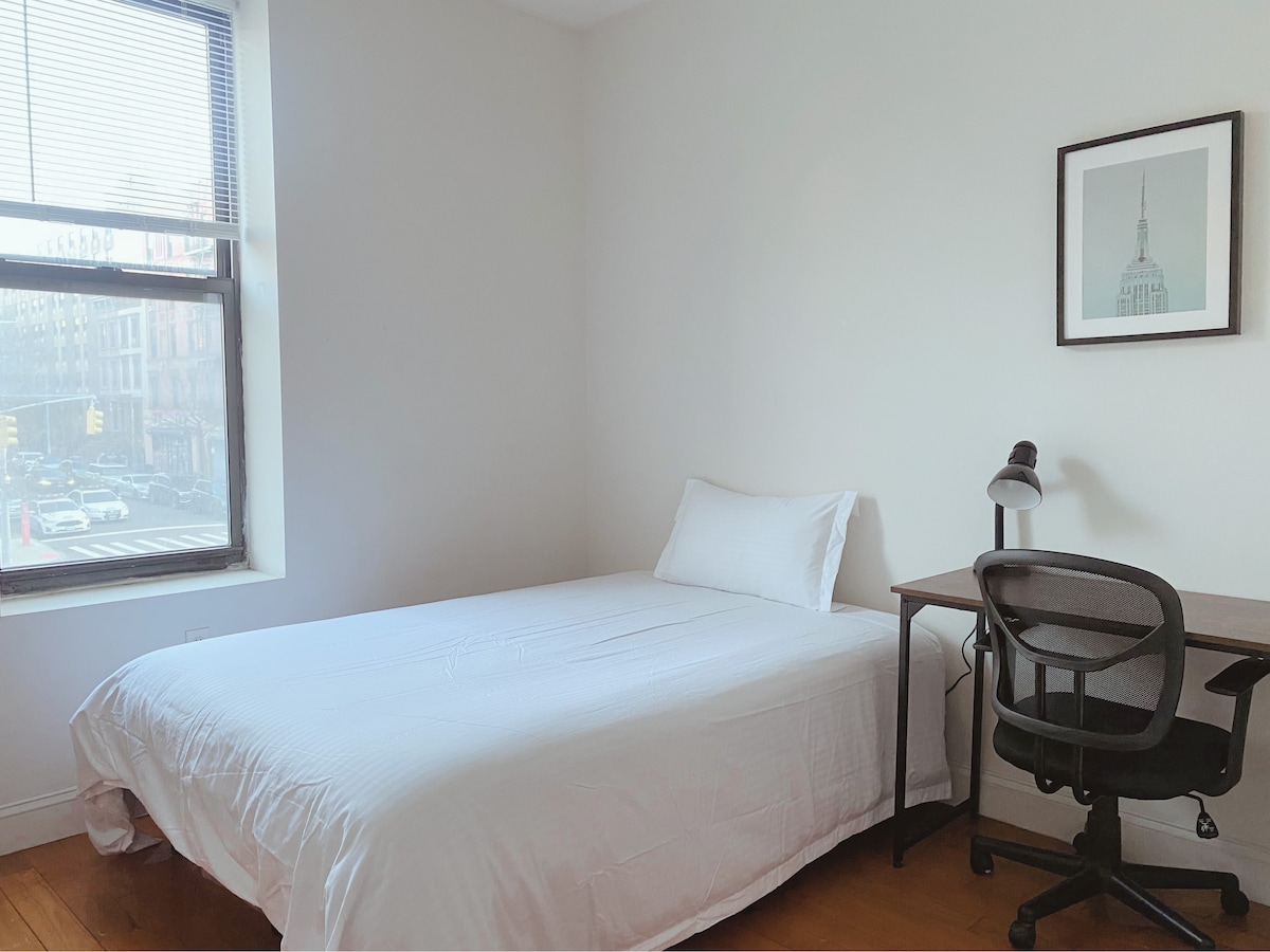 חדר שינה עם מיטה זוגית עם מצעים נקיים, שולחן וכיסא אידיאליים להתקנת WFH ומנורה, המציע מרחב נעים ורגוע.