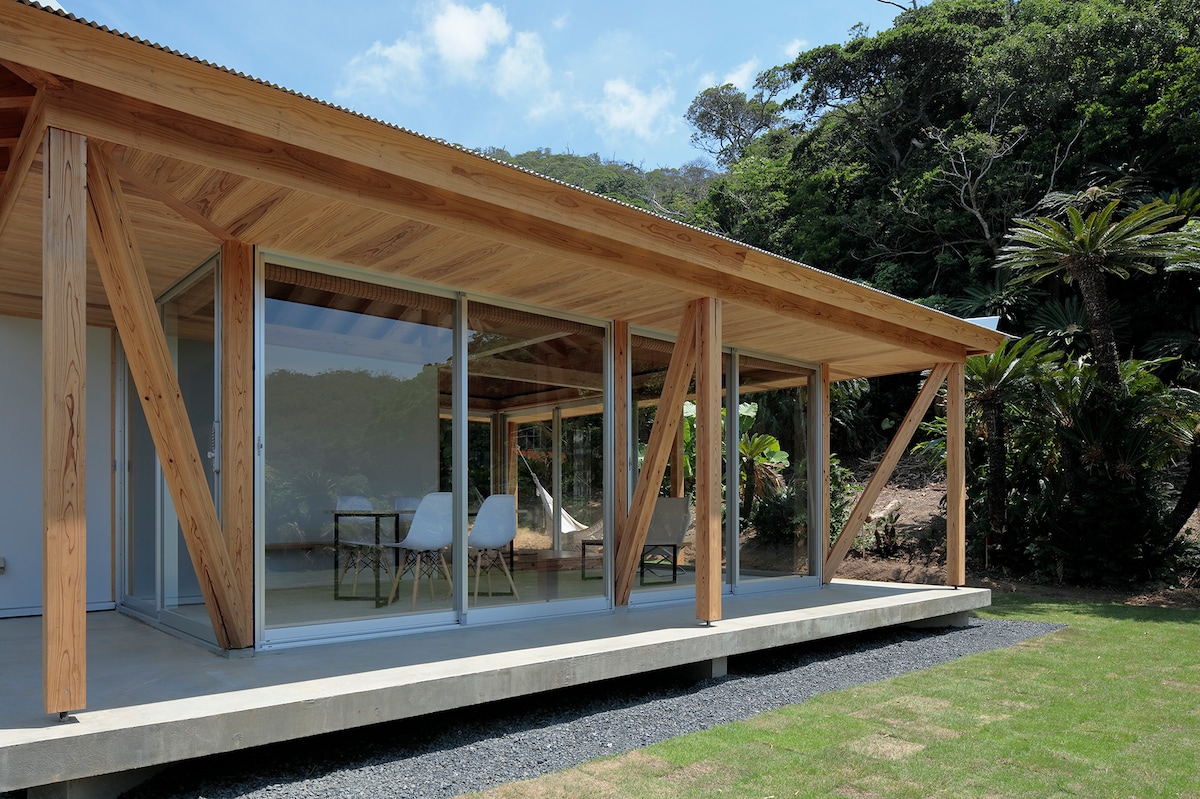 The exterior of a contemporary villa is highlighted, featuring wooden beams and large glass panels that enhance the connection to the surrounding nature. A well-maintained lawn and tropical landscaping create a serene environment, inviting guests to enjoy the outdoor space.