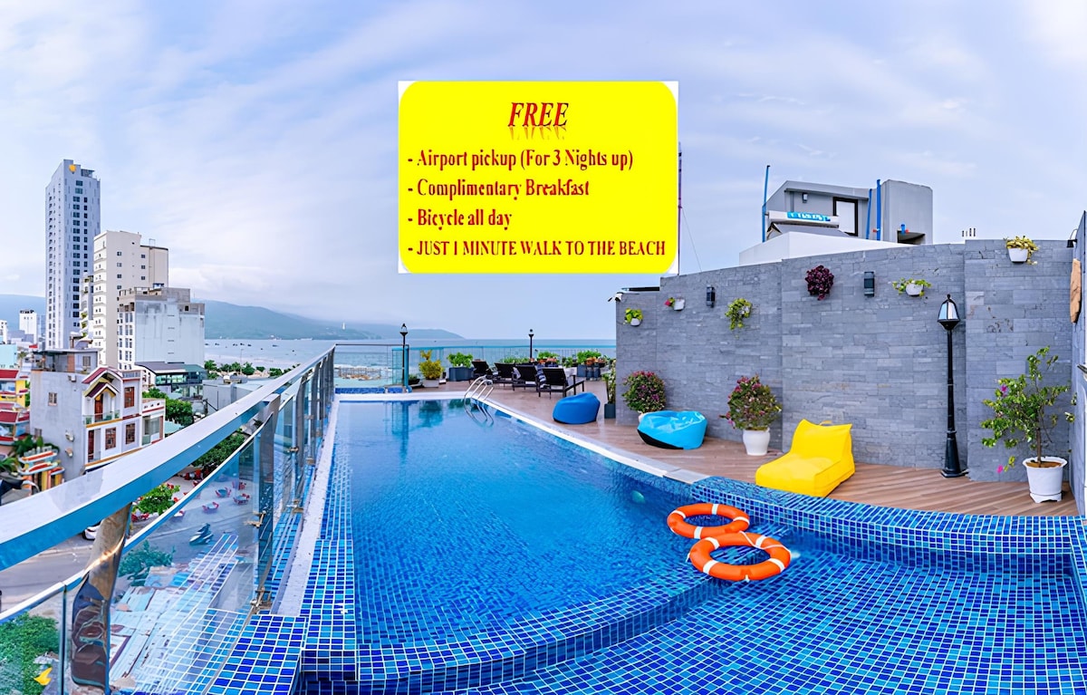 A rooftop pool area is depicted, featuring colorful floatation devices resting on the water's surface. Surrounding lounge chairs and small planters with greenery are visible against a backdrop of coastal views. Informational text highlights complimentary services and proximity to the beach.