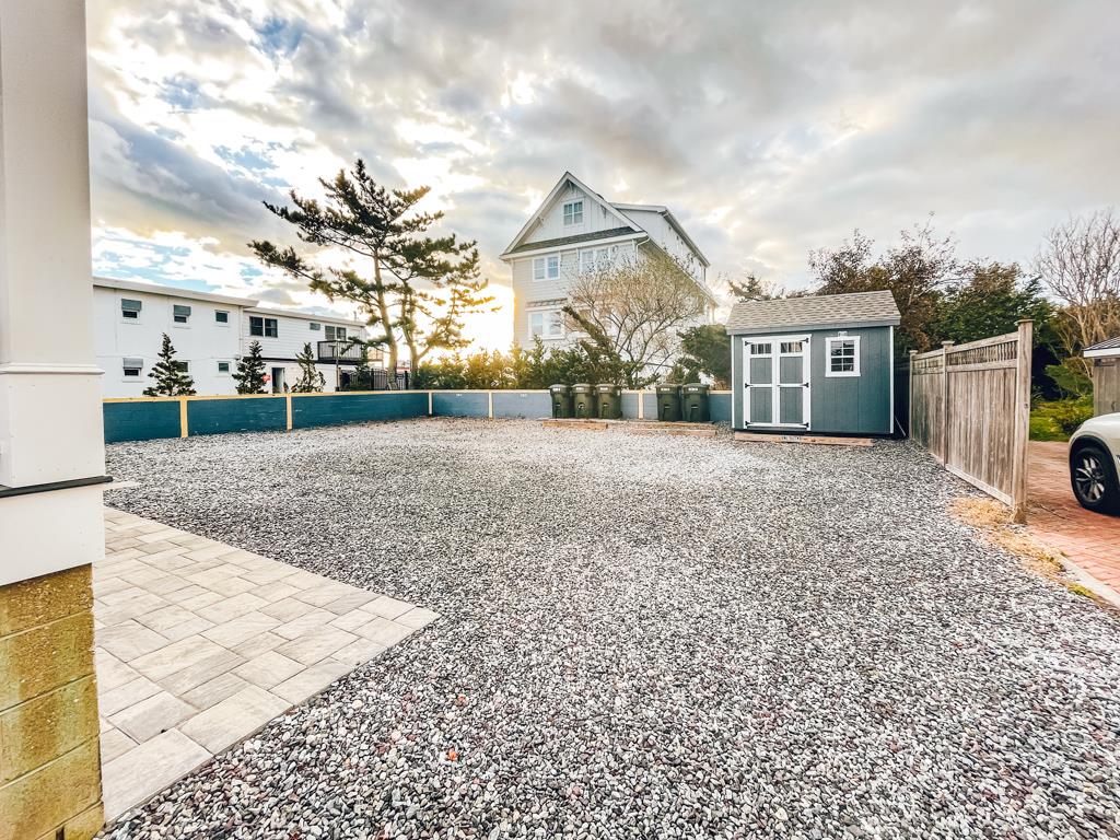 A spacious outdoor area is covered with gravel, providing ample parking space. In the background, a large house and trees are visible, with a shed nestled to one side. The scene is illuminated by soft, natural light under an overcast sky.
