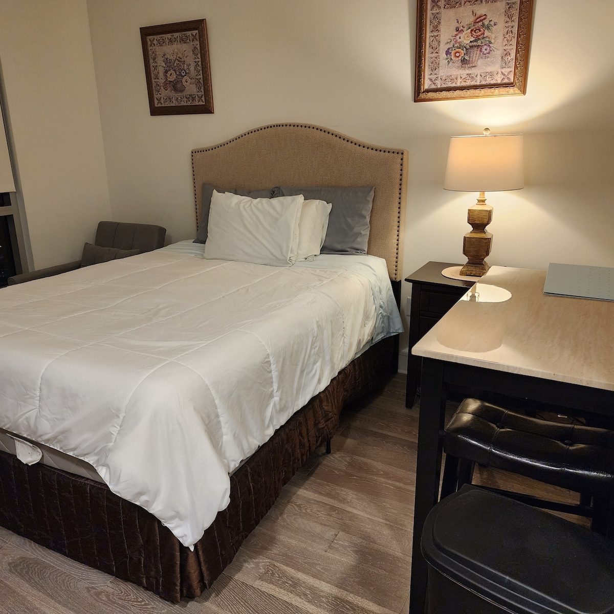 A welcoming sleeping area features a spacious bed dressed with fresh linens and pillows. A bedside lamp provides soft lighting, and a small table stands nearby. A comfortable seating area is also visible, enhancing the room's functionality.