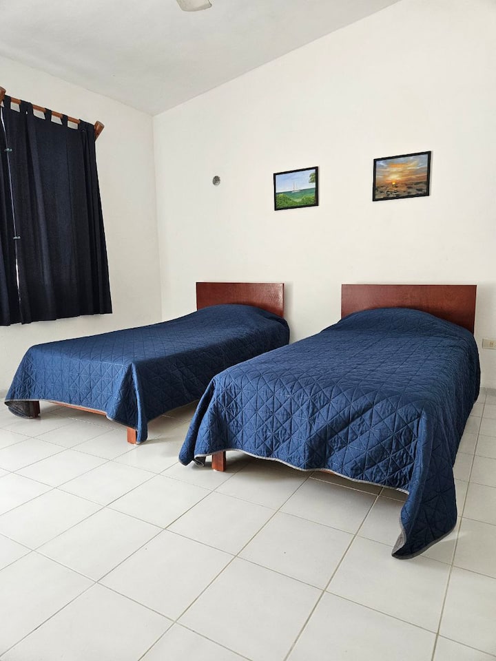 Dve jednolôžka, malý stolík, veľká skriňa na uloženie oblečenia. Stropný ventilátor a klimatizácia. Táto spálňa sa nachádza na druhom poschodí, okno je orientované na pláž. Má dvere na výstup na terasu. 