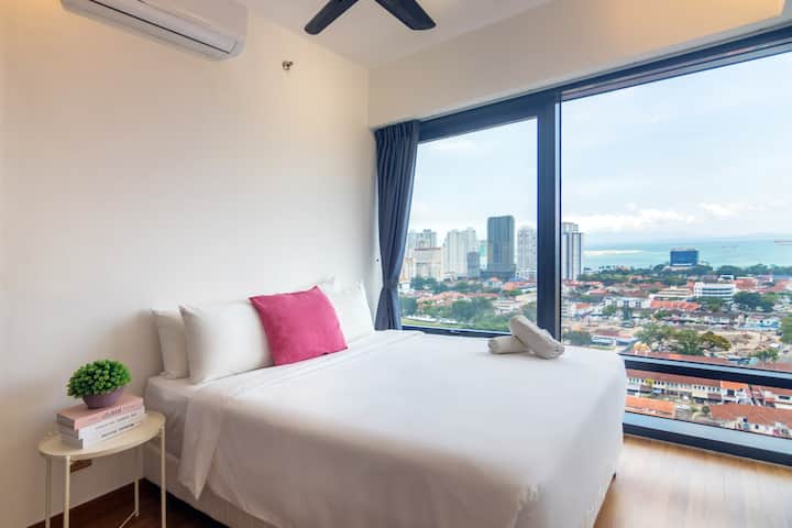This modern bedroom features a luxurious King Koil bed, ample natural light from large windows showcasing the city and sea.