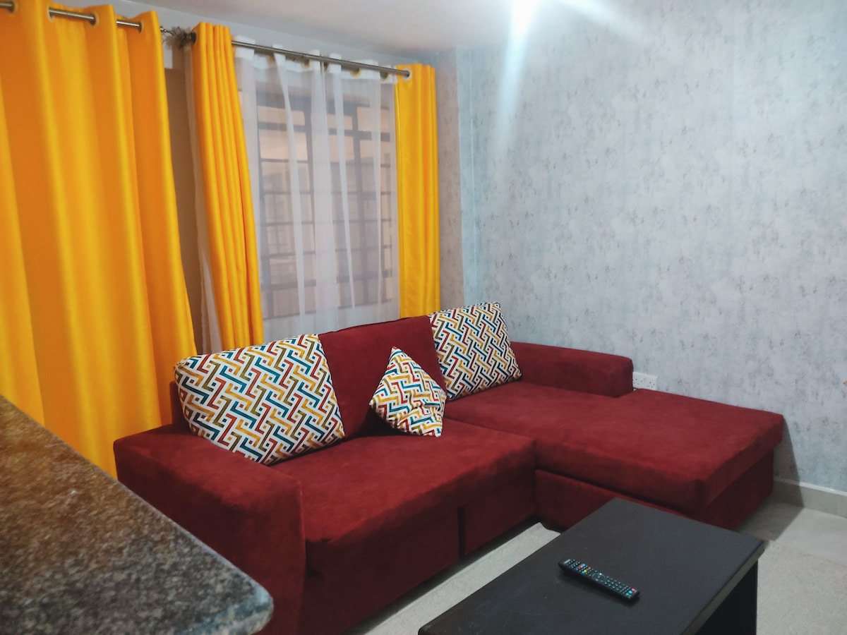 A comfortable seating area features a deep red sectional sofa adorned with patterned throw pillows. Bright yellow curtains frame the window, allowing natural light to brighten the space. A dark coffee table sits in the center, offering a functional surface for relaxation.
