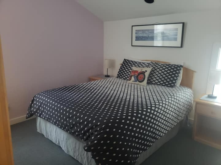 Chumba kikuu cha kulala kilicho na kitanda cha ukubwa wa malkia, meza mbili ndogo, taa mbili, simu ya mstari wa ardhi, saa ya king 'ora, kabati la nguo na kitengo cha AC/ Heater.