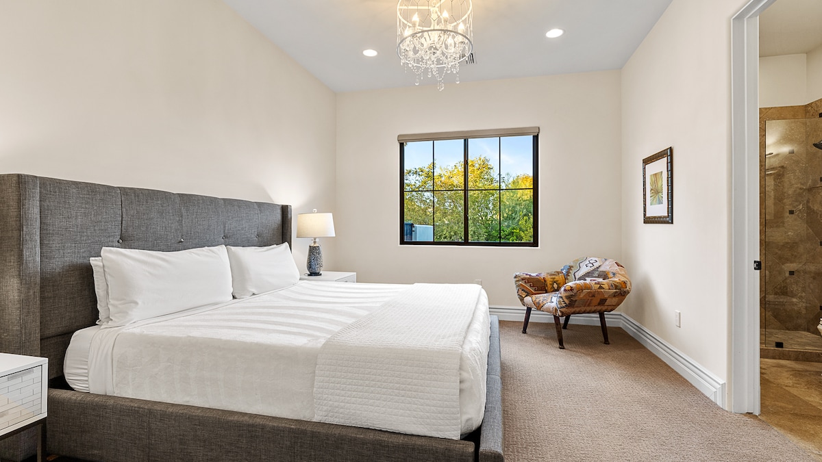 Moderná spálňa s plyšovou čalúnenou posteľou, vlastnou kúpeľňou a prirodzeným svetlom pre pokojné útočisko.