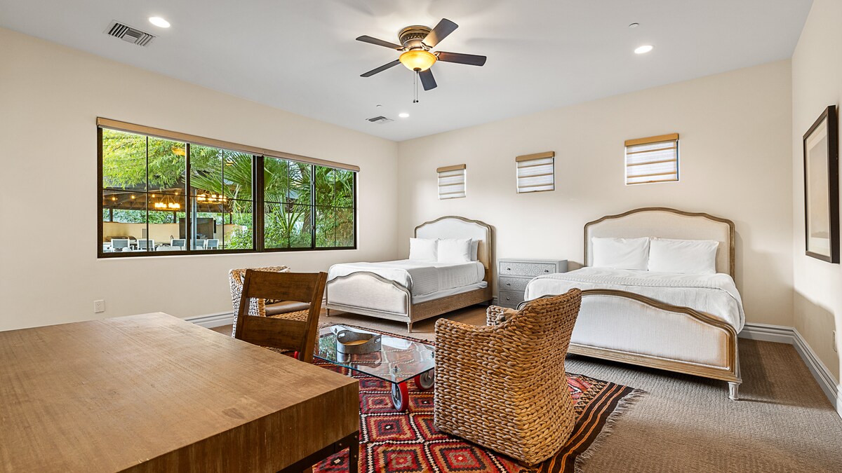 Priestranná spálňa s dvoma elegantnými posteľami, útulným posedením a veľkými oknami s výhľadom na bujnú zeleň.