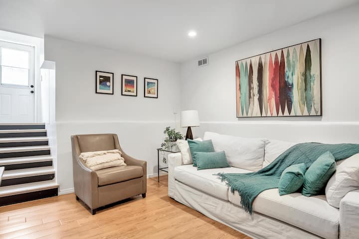 Scopri il comfort e lo stile nel nostro accogliente soggiorno al piano di sotto, con un morbido divano, libri e un grande schermo TV.