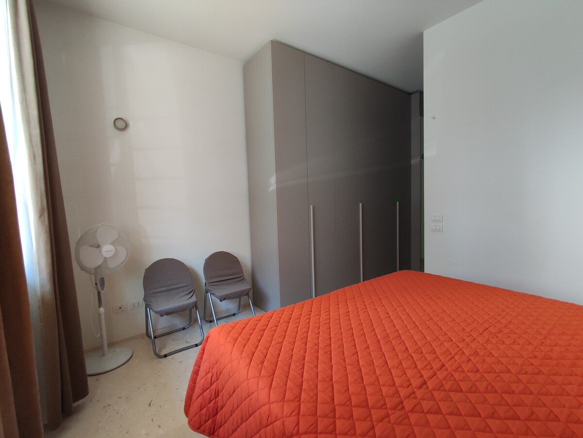 Chumba cha kulala kina kitanda cha watu wawili na kabati lenye milango minne, feni na viti viwili.