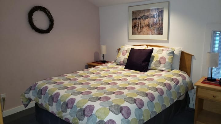 Chambre principale de la suite avec lit queen, deux petites tables, deux lampes, un téléphone fixe, un réveil, une armoire et un climatiseur.
