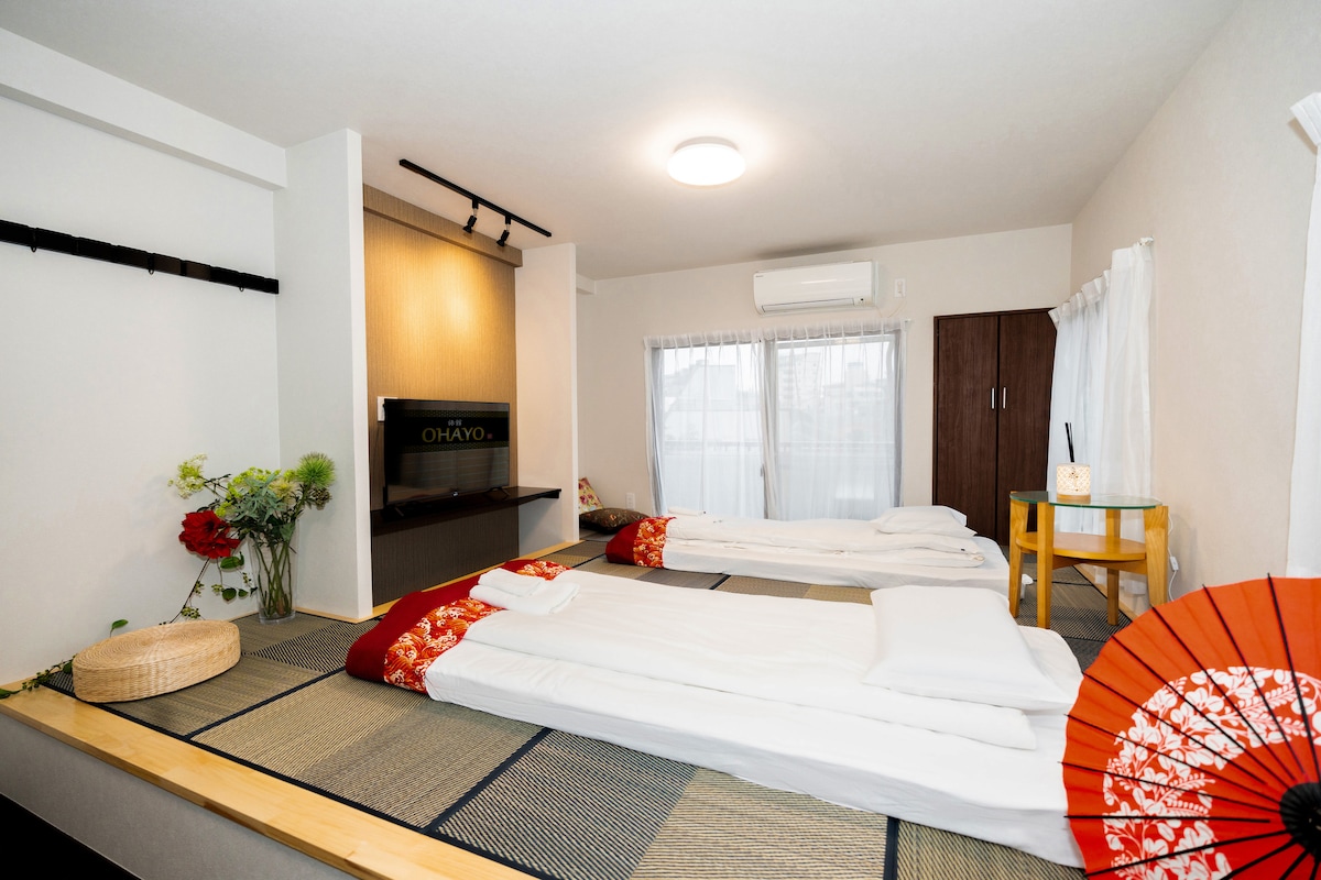 Japanese-style bedroom with two futons on tatami mats, a wall-mounted TV, and a traditional red umbrella.