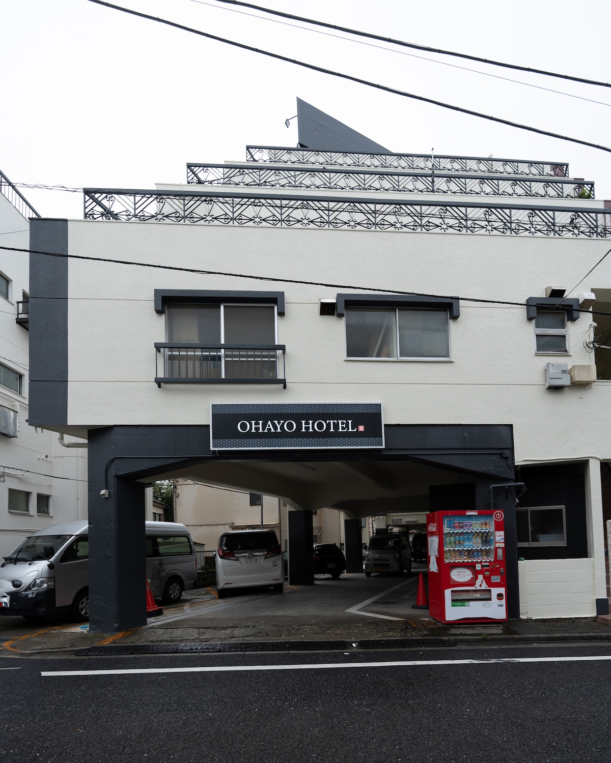 Exterior of a white and grey hotel building with a covered parking area and a red vending machine.