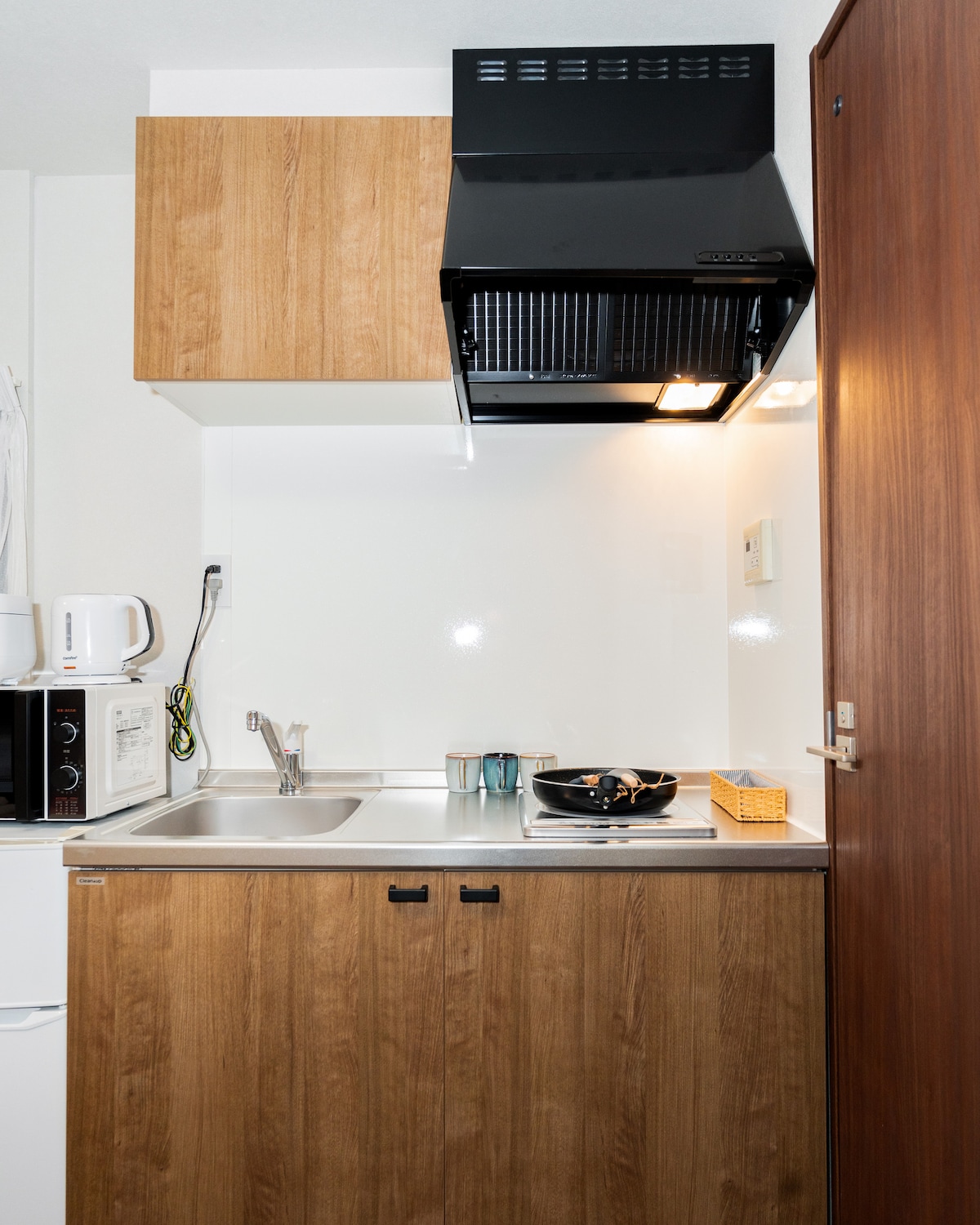 Compact kitchenette with wooden cabinets, stainless steel sink, single stove burner, and black range hood.