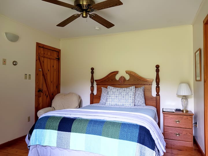 Wild Yam features one queen-sized bed and a private full bathroom with a bathtub. The room includes two bedside tables, as well as another table and chair for seating. 