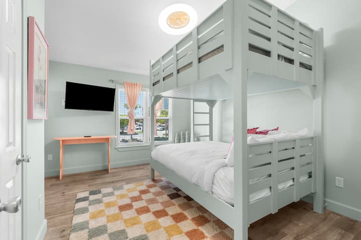 Say hello to the coolest kid (or adult!) space around. A mint green queen bunk bed setup with fun pops of pink and a smart TV—perfect for winding down.