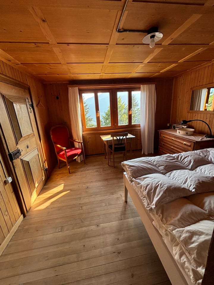 חדר שינה בקומה 1 עם מיטה זוגית, כורסה, שולחן, שידת מגירות ודלת חיבור לסלון.