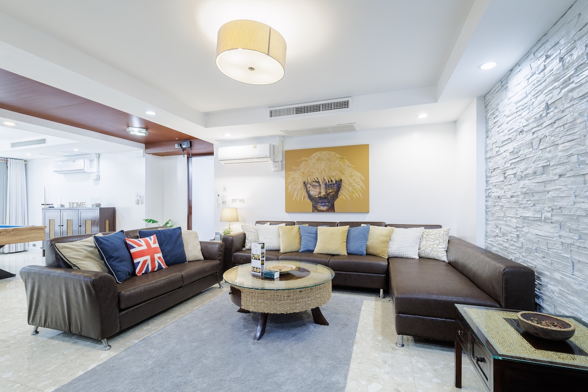A spacious living area is shown, featuring a dark sectional sofa adorned with decorative cushions. A round coffee table is centered on a soft area rug, while an art piece hangs on the wall, contributing to the contemporary design. Soft lighting enhances the overall ambiance.