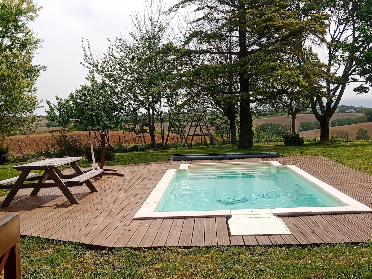 A private pool is surrounded by a wooden deck, providing a serene outdoor area. Lush greenery and trees frame the space, complementing the tranquil landscape views. A picnic table is positioned nearby, offering a casual spot for relaxation or dining.