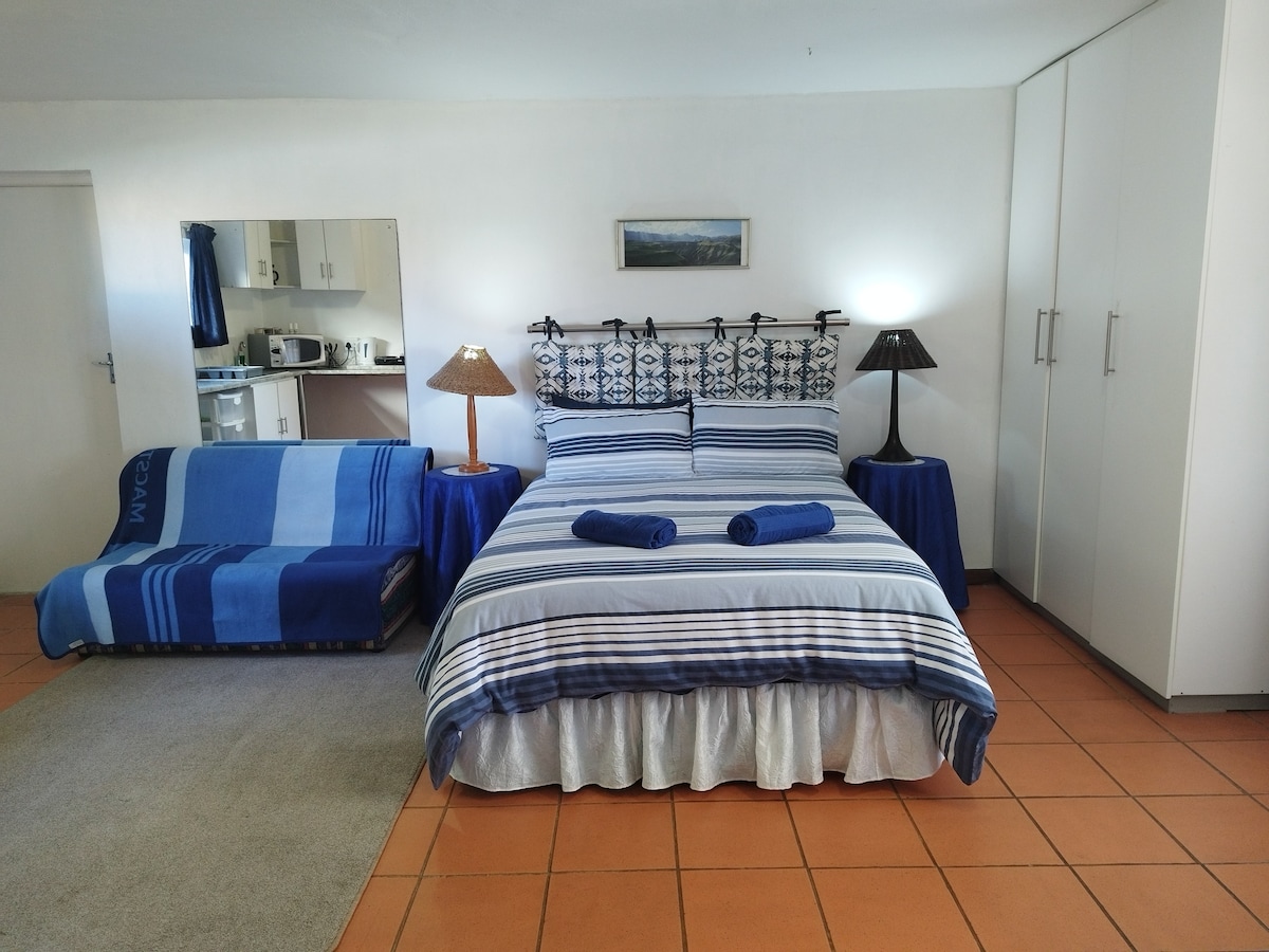 A spacious sleeping area features a large bed with striped bedding, complemented by matching towels. A sofa bed in blue is positioned alongside a nightstand with a lamp. Storage cabinets are present, and a mirror reflects the room's layout.