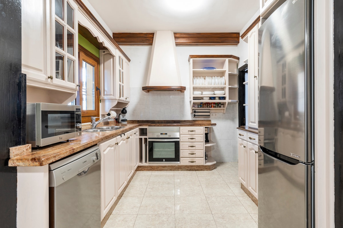 The kitchen features a combination of light cabinetry and a granite countertop. It is equipped with modern appliances, including a microwave, dishwasher, and refrigerator. Ample storage space is offered with built-in shelves, while large windows provide natural light.
