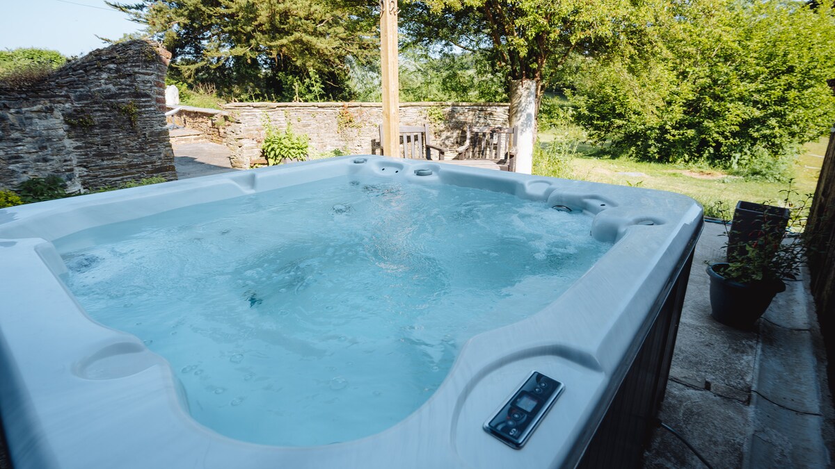 A private hot tub is positioned outdoors near a stone wall, surrounded by greenery. Clear water creates gentle ripples, while nearby plants add a touch of nature. The area is designed for relaxation, enhancing the outdoor experience in a tranquil setting.