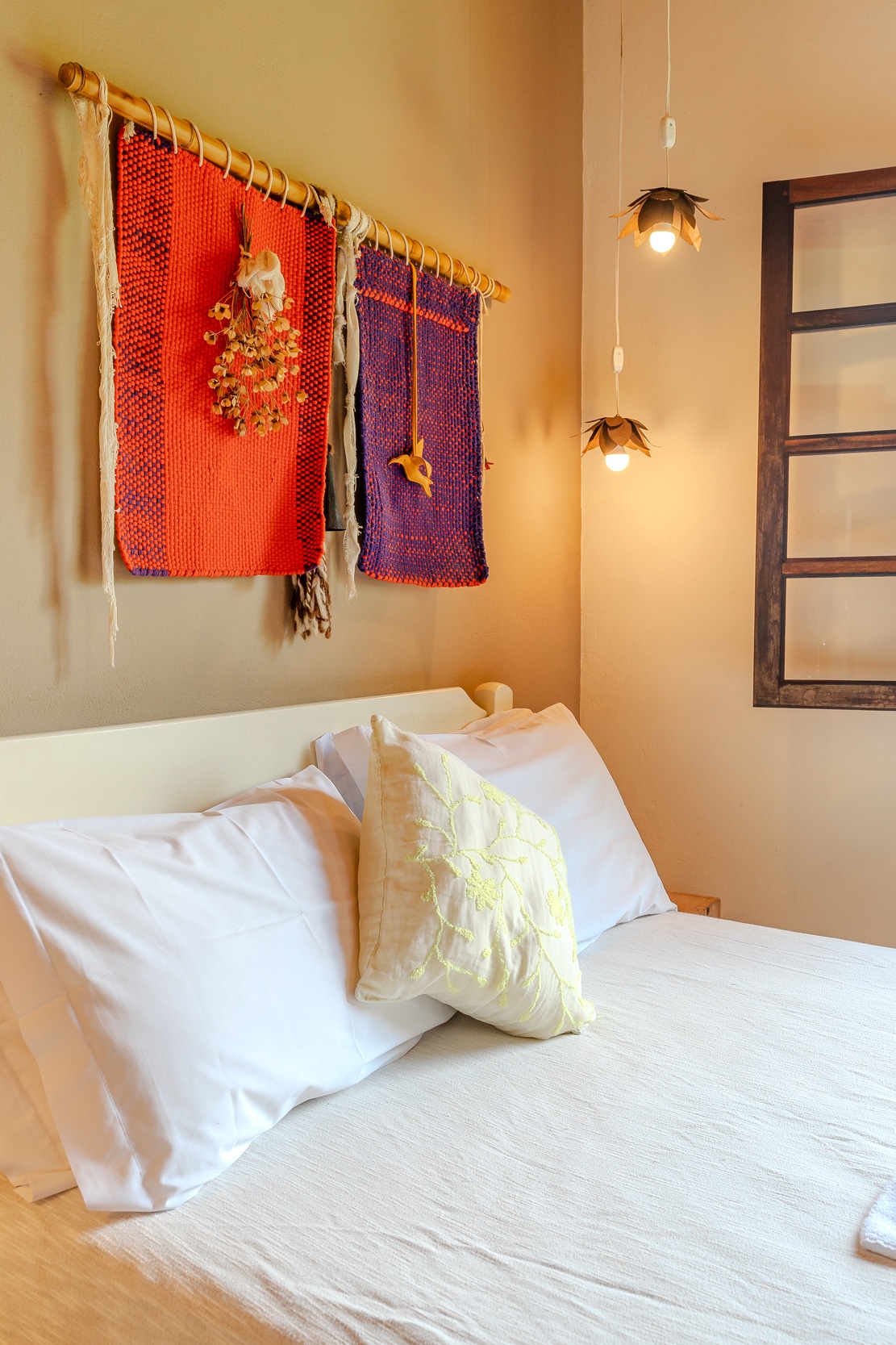 A spacious bed is dressed in crisp white linens, complemented by decorative pillows. Colorful wall hangings in red and blue add visual interest above the bed. Soft pendant lights provide gentle illumination, enhancing the cozy ambiance of the room.