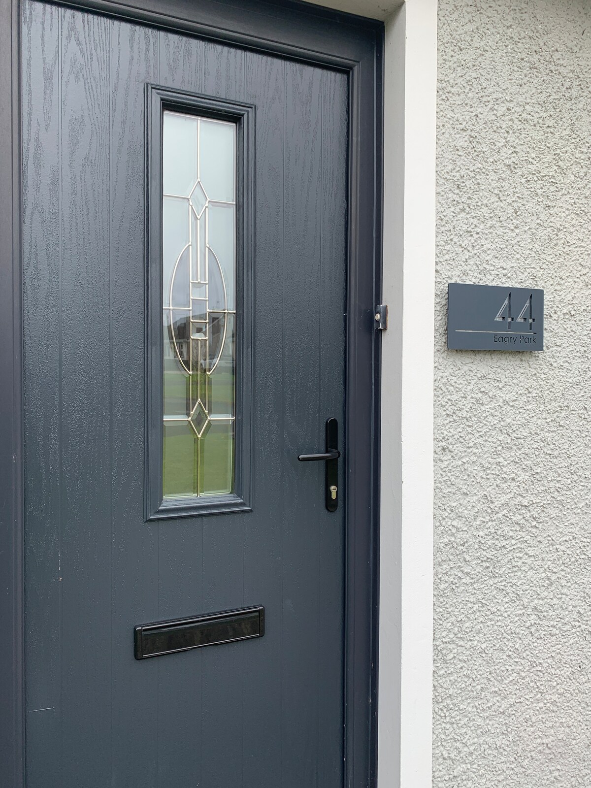 A stylish entrance door features a decorative glass panel along the top, allowing light to filter through. The door is painted in a deep gray hue, complemented by a matching house number plaque mounted beside it, indicating the residence number 44.