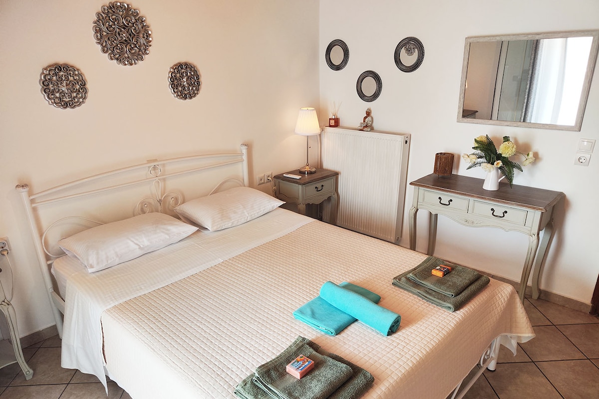 ห้องนอนที่สว่างและน่าอยู่ มีเตียงใหญ่น่านอน ตกแต่งผนังอย่างมีรสนิยม และแสงไฟที่นุ่มนวลเพื่อการเข้าพักที่ผ่อนคลาย การตกแต่งอย่างมีระดับ เช่น ดอกไม้และผ้าขนหนูที่จัดเรียงอย่างประณีตช่วยเพิ่มความรู้สึกอบอุ่น