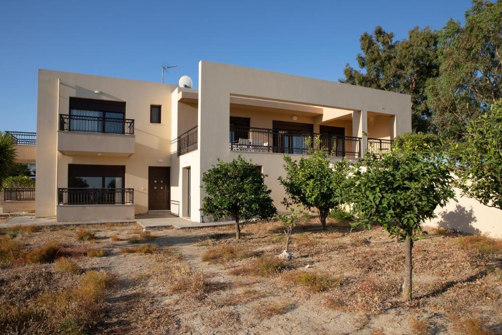 The exterior of Villa Panoramica is shown, featuring a two-story structure with a light-colored facade. Balconies with black railings are visible, along with a front door surrounded by greenery. A clear blue sky illuminates the scene, highlighting the surrounding tranquil landscape.