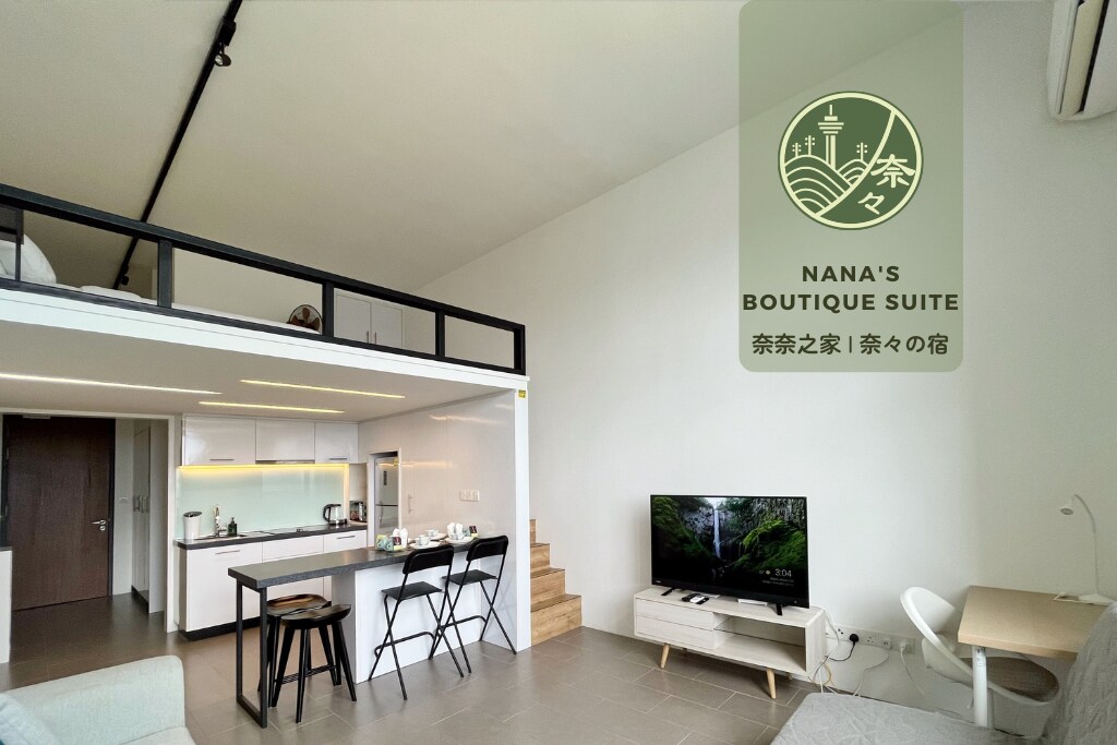 An open-plan loft area is highlighted, showcasing a dining counter with high chairs and a well-equipped kitchen. The living space features a smart TV and a sofa, with steps leading to the loft above. Natural light streams in from large windows, enhancing the overall ambiance.