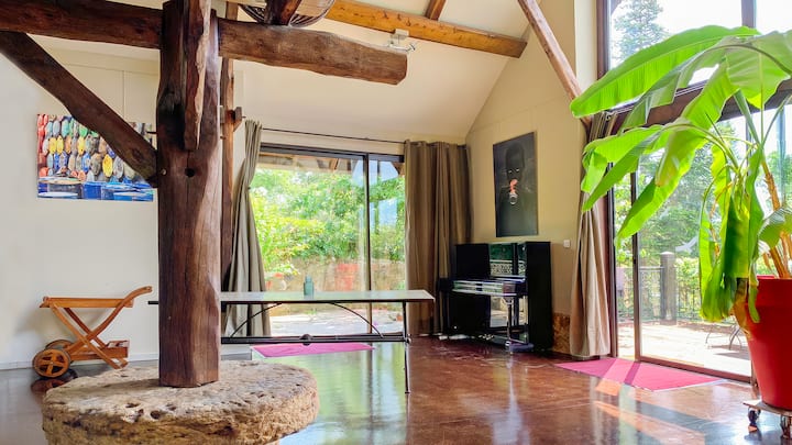 סלון עם תקרות גבוהות, קורות עץ ישנות מקוריות וחלונות מהרצפה עד התקרה. חזית הזכוכית פותחת את החדר לגינה ולמרפסת. פסנתר, תמונות שונות ושולחן אוכל גדול מציעים שפע של מקום להירגע