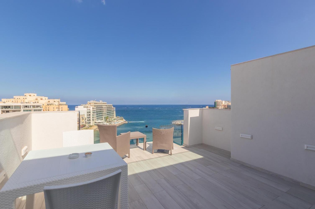 A spacious private roof terrace is highlighted, featuring a small dining table with chairs and two lounge chairs. The unobstructed views of the sea and coastline create a serene backdrop, while the tiled flooring complements the modern design.
