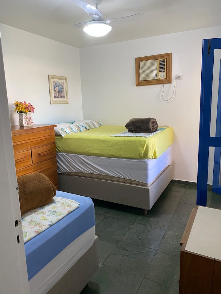 Sala social en el segundo piso. Tiene 1 cama doble, 1 cama individual, ventilador y aire acondicionado. A la derecha, puerta de acceso al balcón del dormitorio.