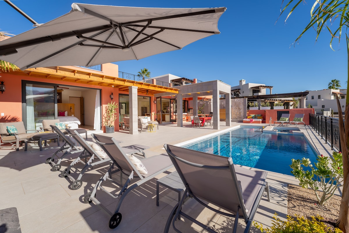 The outdoor area features a private heated pool surrounded by modern lounge chairs, offering a sun-soaked space for relaxation. An umbrella provides shade, while the adjoining patio includes seating arrangements and a well-maintained landscape, contributing to an inviting outdoor environment.
