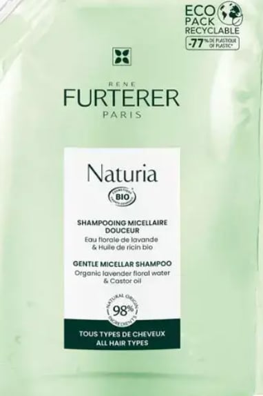 A gently designed shampoo packaging features a pale green background, showcasing the product name 'Naturia' prominently. The label indicates it is a gentle micellar shampoo with organic lavender floral water and castor oil, suitable for all hair types. Eco-friendly packaging details are included.