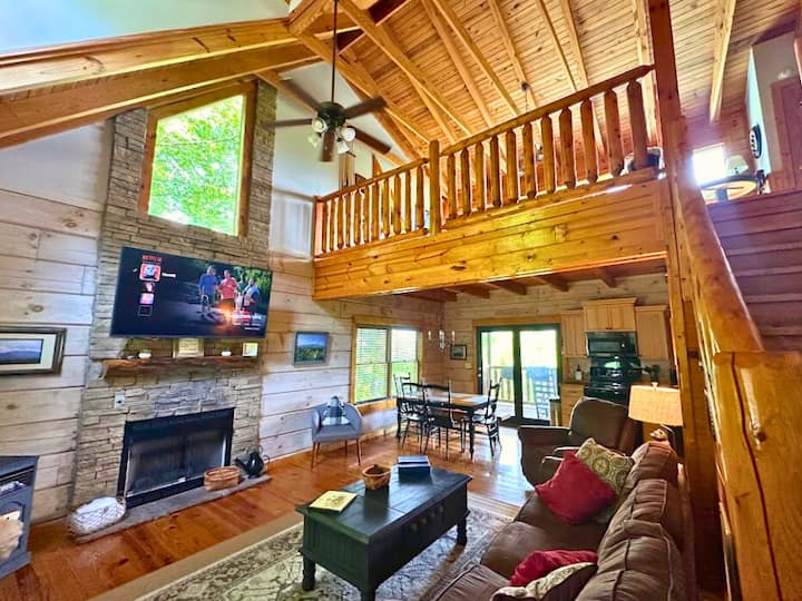 غرفة معيشة واسعة ذات تصميم مفتوح مع أسقف مقببة ومدفأة حجرية.