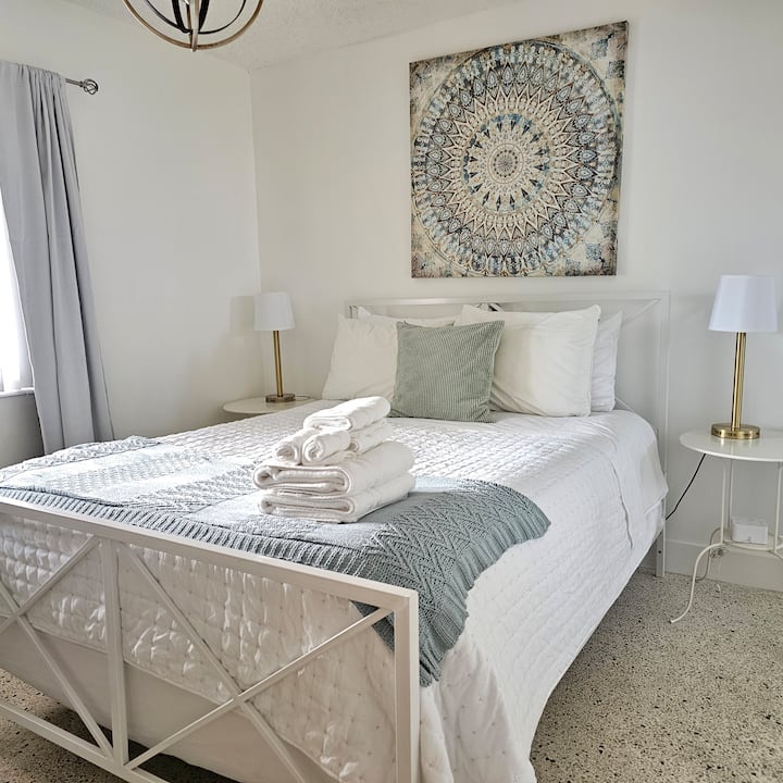 Priestranná a svetlá spálňa s manželskou posteľou s bielou posteľnou bielizňou, zvýraznená jemnými tónmi pre relaxačnú atmosféru. 