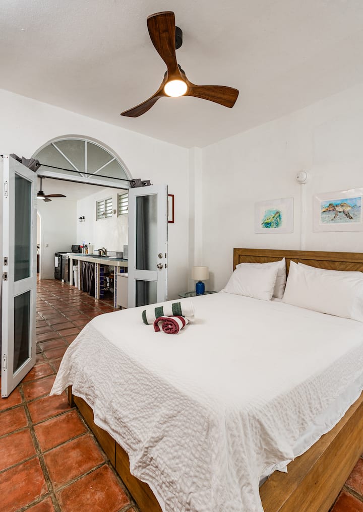 Cozy bedroom with queen bed and crisp white linens, located just off the kitchen. Features a Jack-and-Jill ensuite bathroom connecting to a second bedroom. Enjoy cool, restful nights with brand-new AC—perfect after a warm beach day.