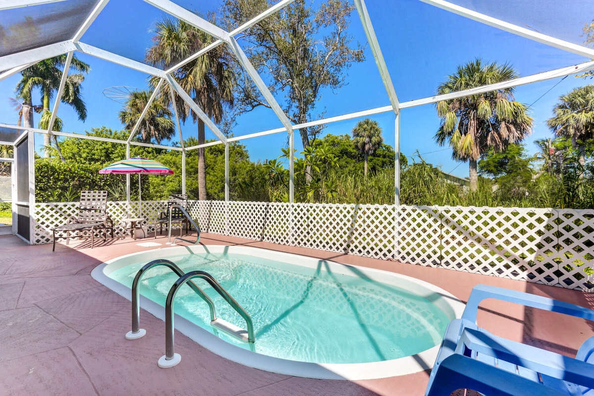 A private screened-in pool area is surrounded by lush greenery and palm trees, creating a serene atmosphere. Lounge chairs are positioned nearby, and the pool features steps leading into the clear water. Bright sunlight streams through the enclosure, enhancing the inviting space.