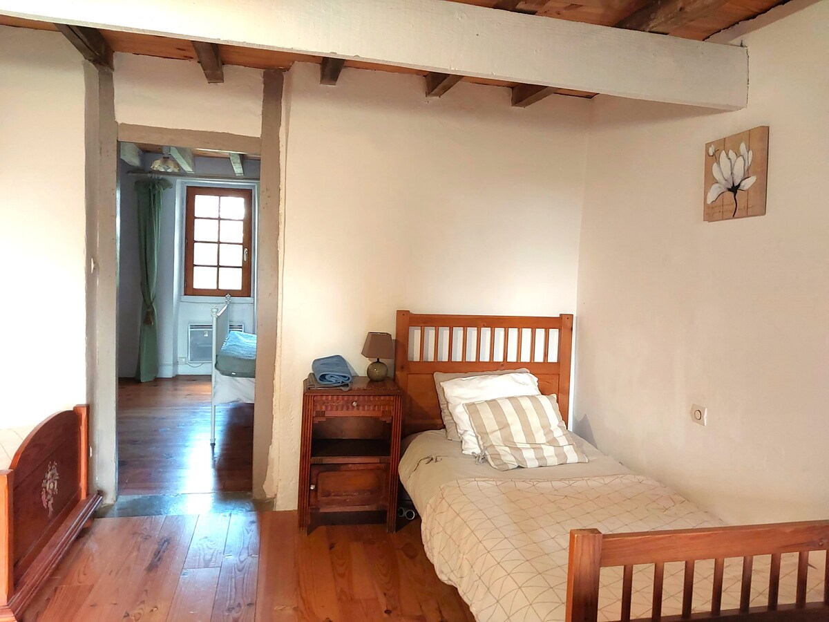 Children's or friends' room with 3 single beds, exposed beams, parquet, small easel table, plaid, and wardrobe.