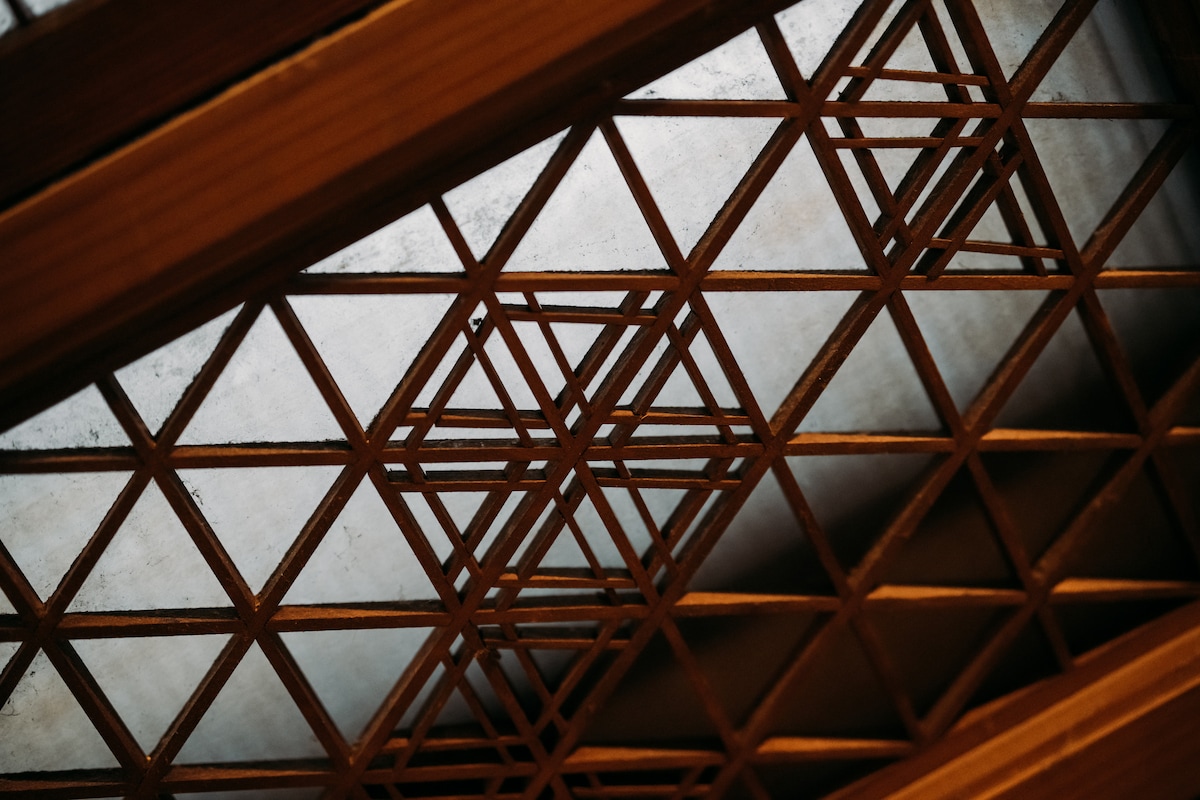Intricate wooden latticework is featured in the ceiling, showcasing a geometric pattern that allows soft light to filter through. The craftsmanship is highlighted by the contrasting textures between the wood and the illuminated space above.