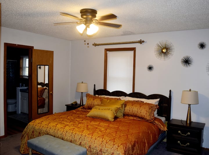 Დიდი საწოლი შესასვლელი კარადით, ორი ღამის თაროებით, კომოდითა და ტელევიზორით.  