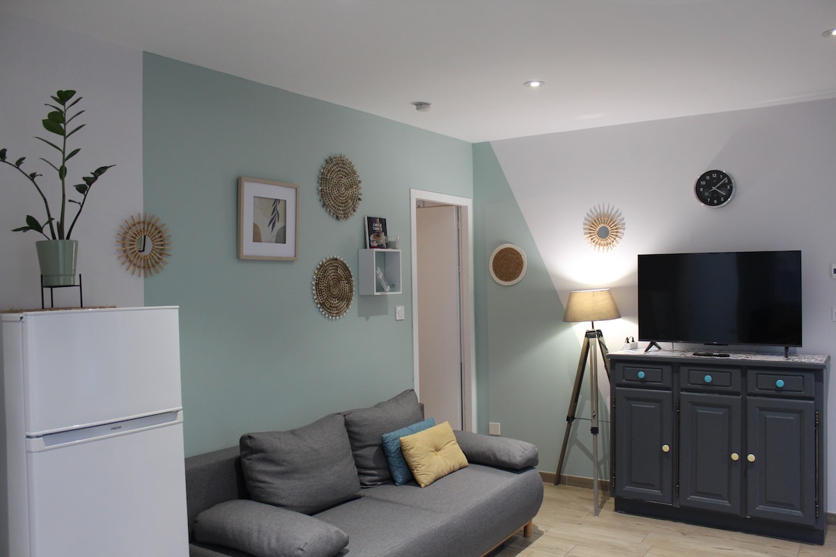 A living area showcases a comfortable gray sofa with decorative cushions, complemented by a sleek white refrigerator. A wall-mounted television is positioned next to a stylish sideboard. Framed art and wall decor add a touch of elegance, with a soft lamp providing ambient lighting.