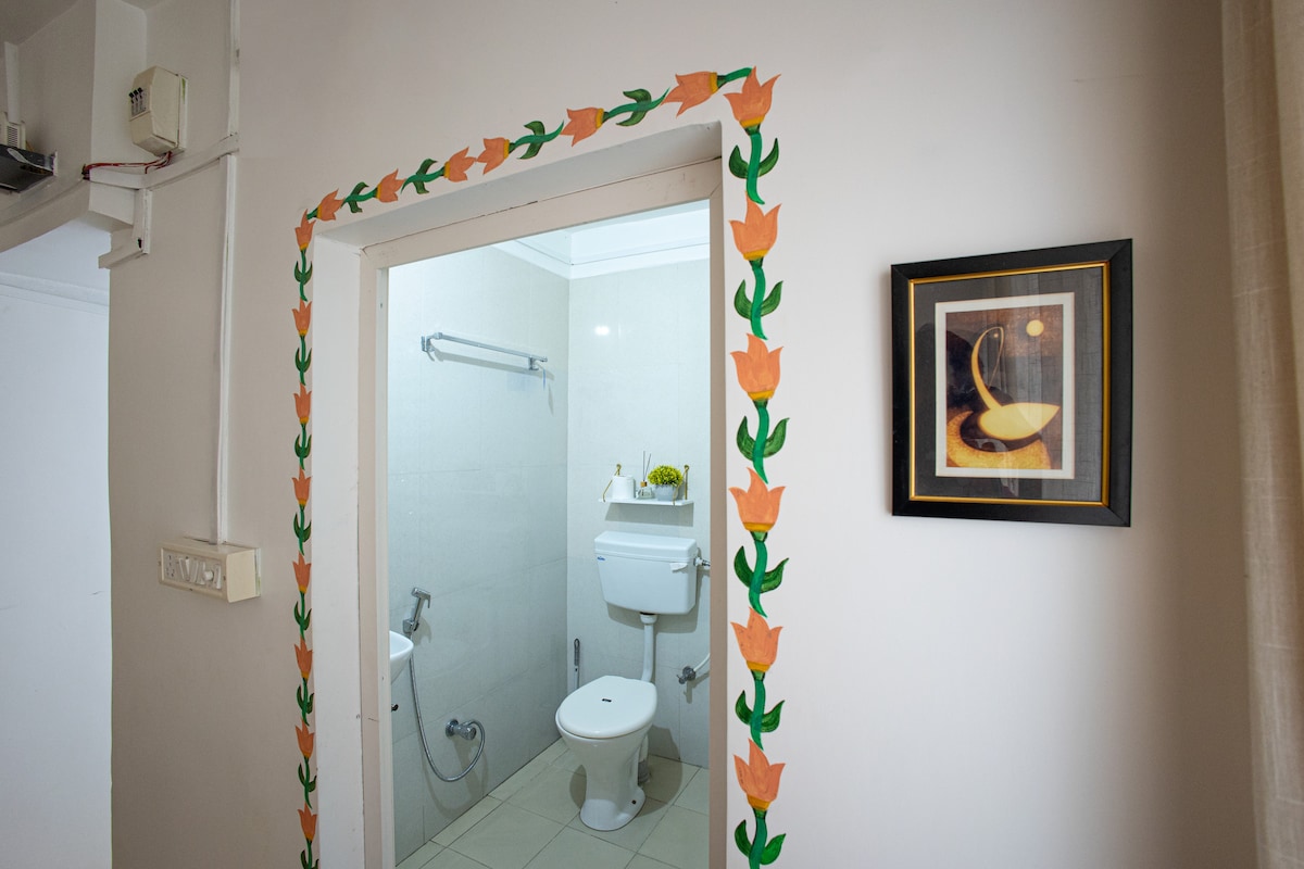 The bathroom entrance is framed with floral decor, adding a touch of color to the wall. Inside, a white toilet and sink are visible, complemented by a shower fixture. A framed artwork hangs nearby, enhancing the overall aesthetic of the space.