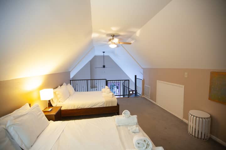 Un espacioso dormitorio tipo loft en la planta superior con dos camas tamaño matrimonial y un acogedor rincón de lectura. Este espacio abierto es ideal para huéspedes adicionales o niños, ya que ofrece privacidad sin dejar de estar conectado a la sala de estar principal.