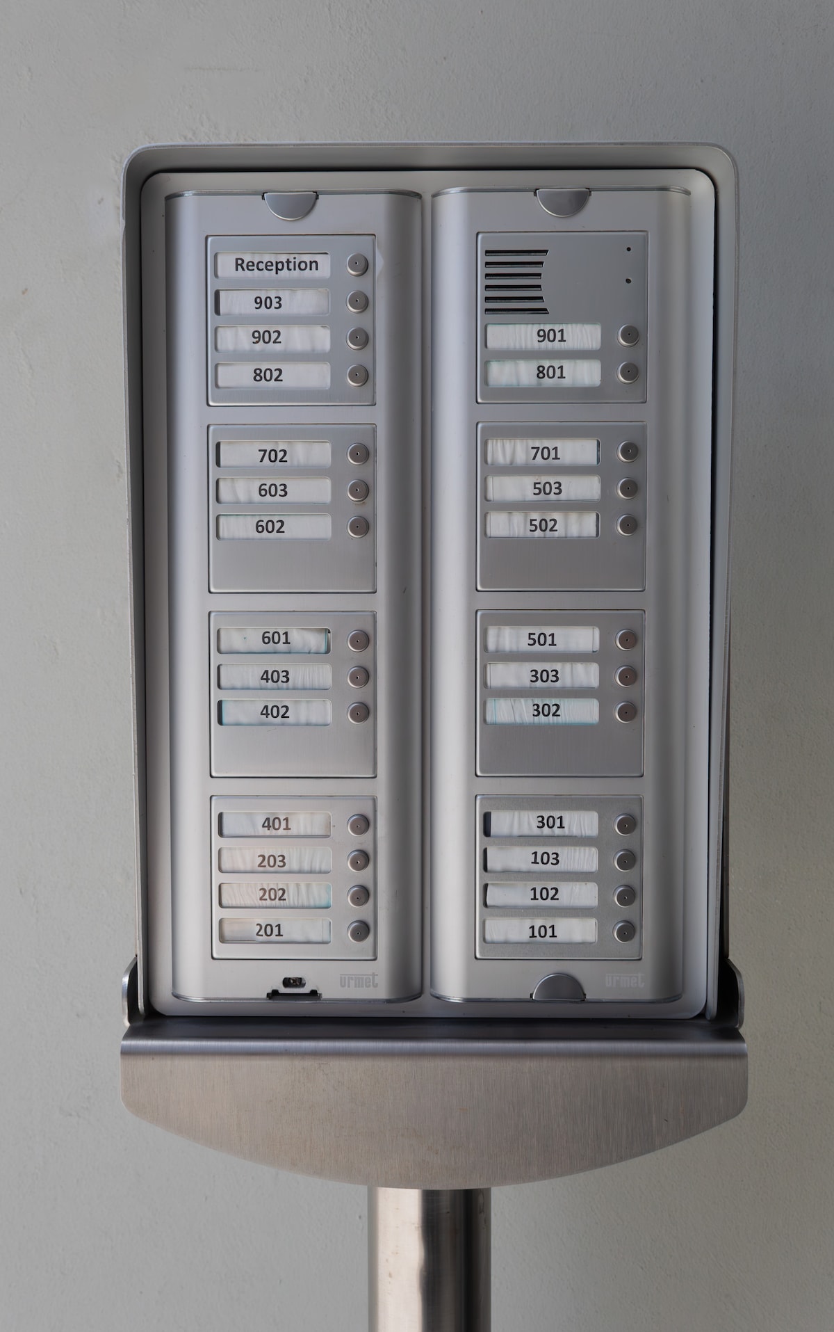 A modern intercom system is displayed, featuring a grid layout with labeled buttons for various unit numbers, including a reception area. The design is clear and organized, facilitating easy communication for guests and residents.