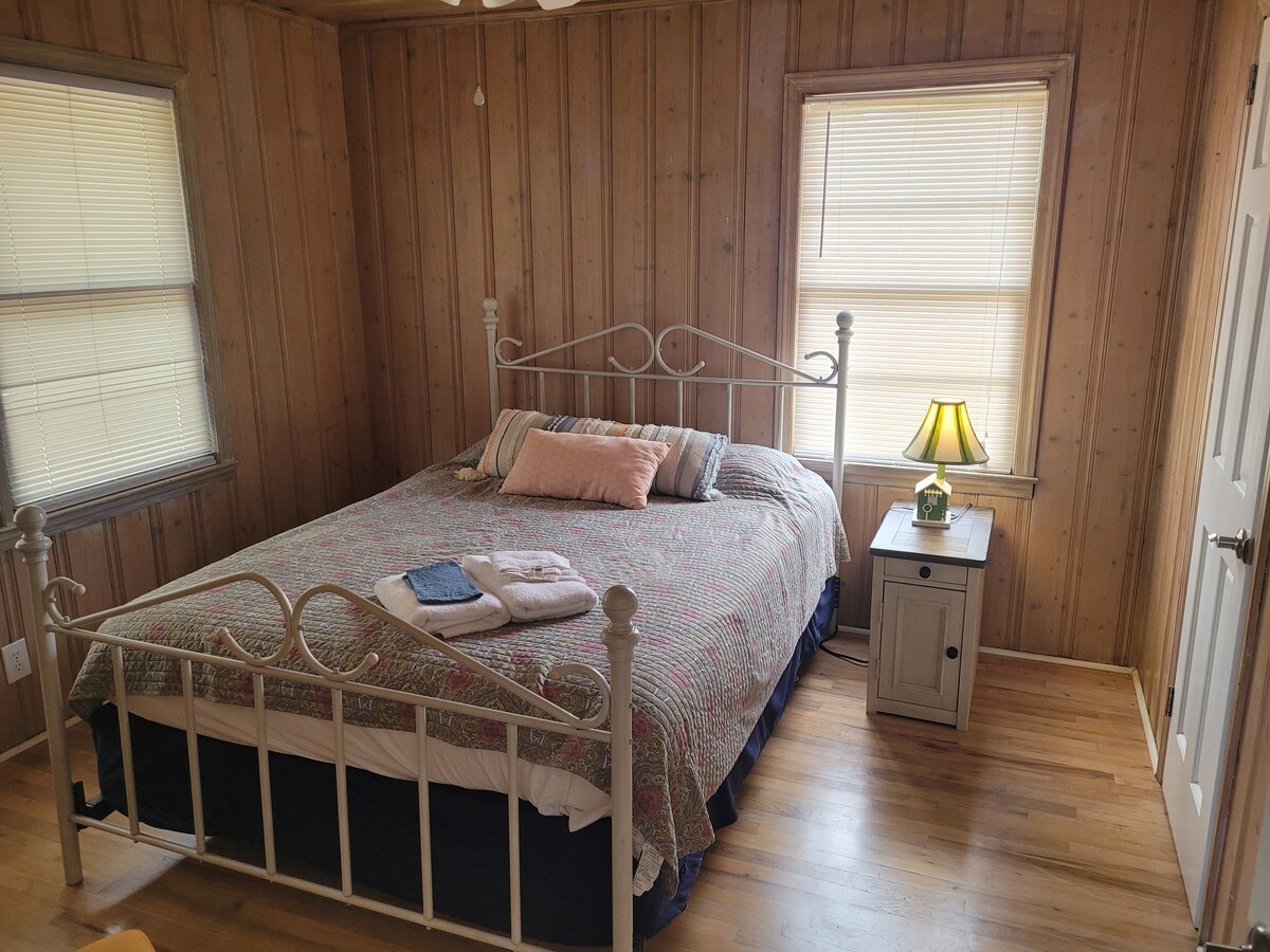 เตียงขนาดควินไซส์พร้อมโต๊ะข้างเตียงที่คุณสามารถใช้เสียบโทรศัพท์ได้ เก้าอี้และตู้เสื้อผ้าเดียวกันพร้อมไม้แขวนเสื้อสำหรับเสื้อผ้าของคุณและครอบครัว