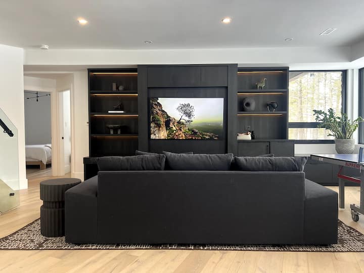 ห้องพักผ่อนชั้นล่างพร้อมทีวีกรอบรูปขนาดใหญ่ ชุดวางสื่อแบบกำหนดเอง โต๊ะปิงปอง และโซฟาให้นอนสำหรับผู้เข้าพักเสริม