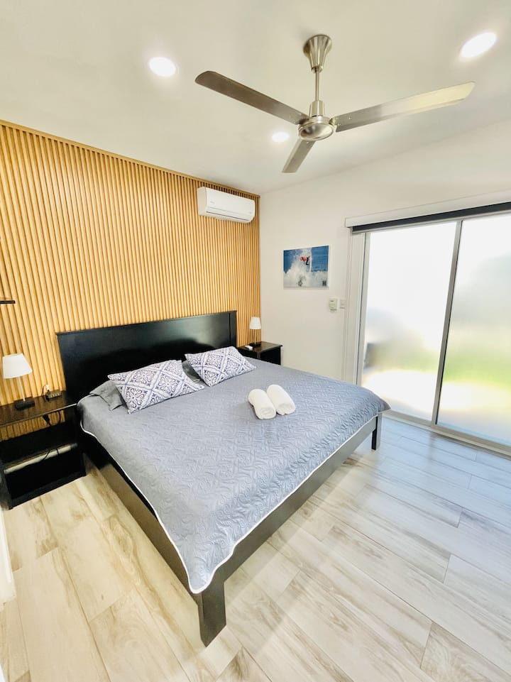 Მშვიდი ძირითადი საძინებელი კონდიციონერით, ჭერის ვენტილატორით და დიდი ზომის საწოლით. Ოთახის გამუქებული ფერები უზრუნველყოფს მშვიდ ძილს. Კარები ღიაა აყვავებულ ბაღში და მოაქვს ბუნებრივი სინათლე და ტროპიკული ნიავი. Სააბაზანო ხელს უწყობს კონფიდენციალურობასა და კომფორტს.